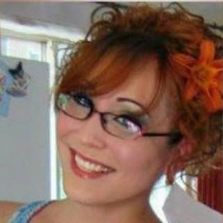 Woman with glasses and orange hair flower smiling indoors.