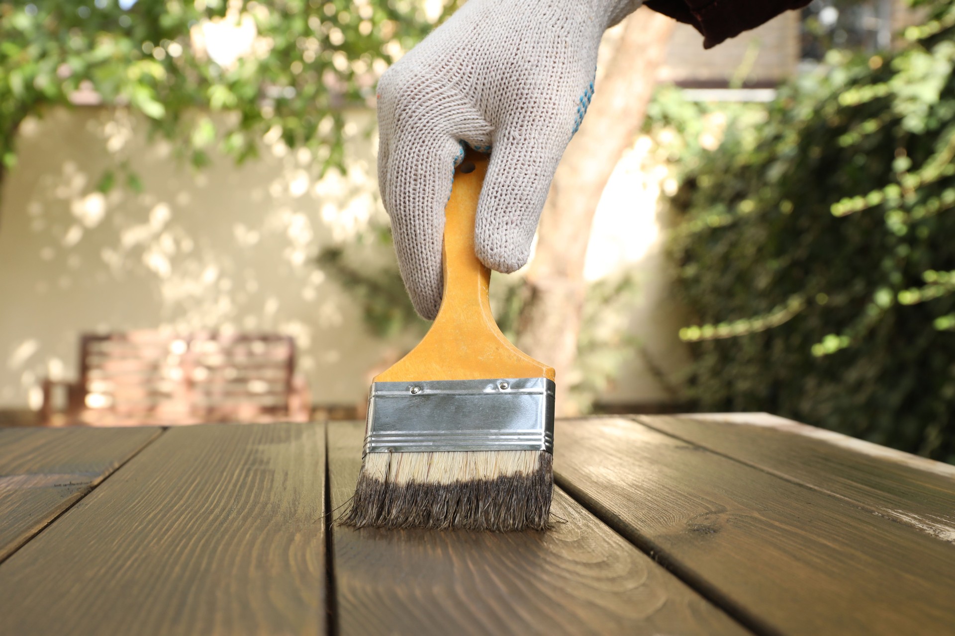 Man applying wood stain onto wooden surface outdoors, closeup. Rejuvenation Renovations